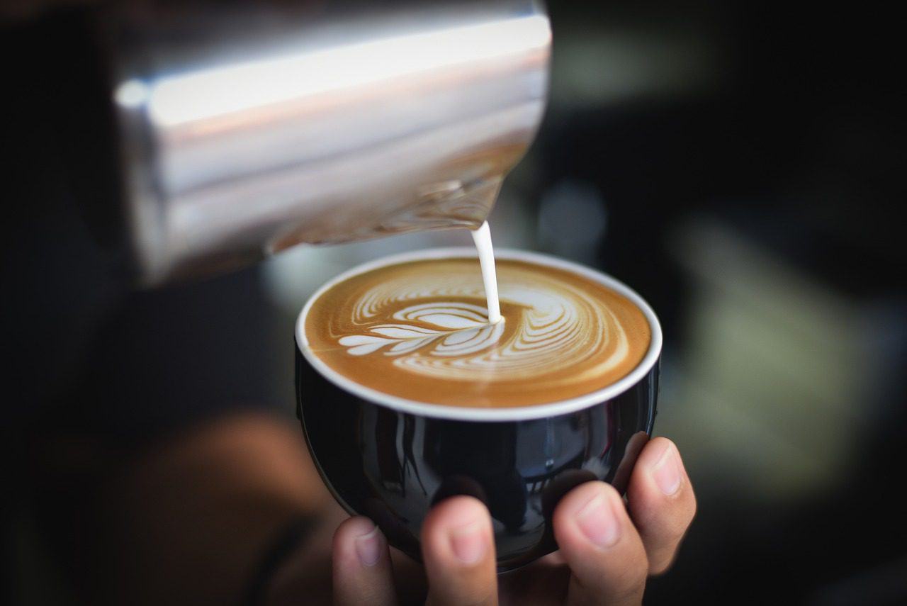 a person pouring milk into a cup of coffee