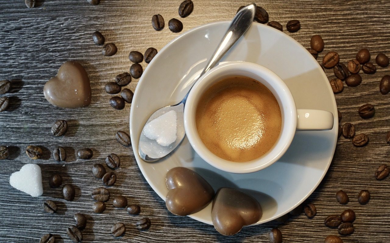 a cup of coffee with a spoon and chocolate hearts on a saucer